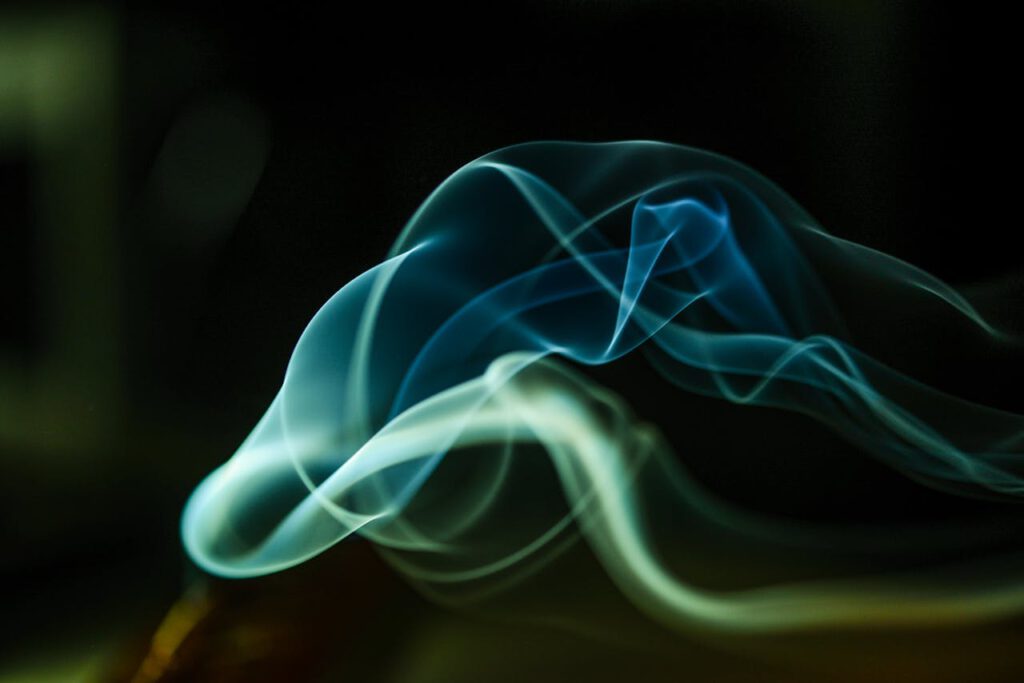 Dynamic smoke waves captured in green and blue hues on a dark backdrop.